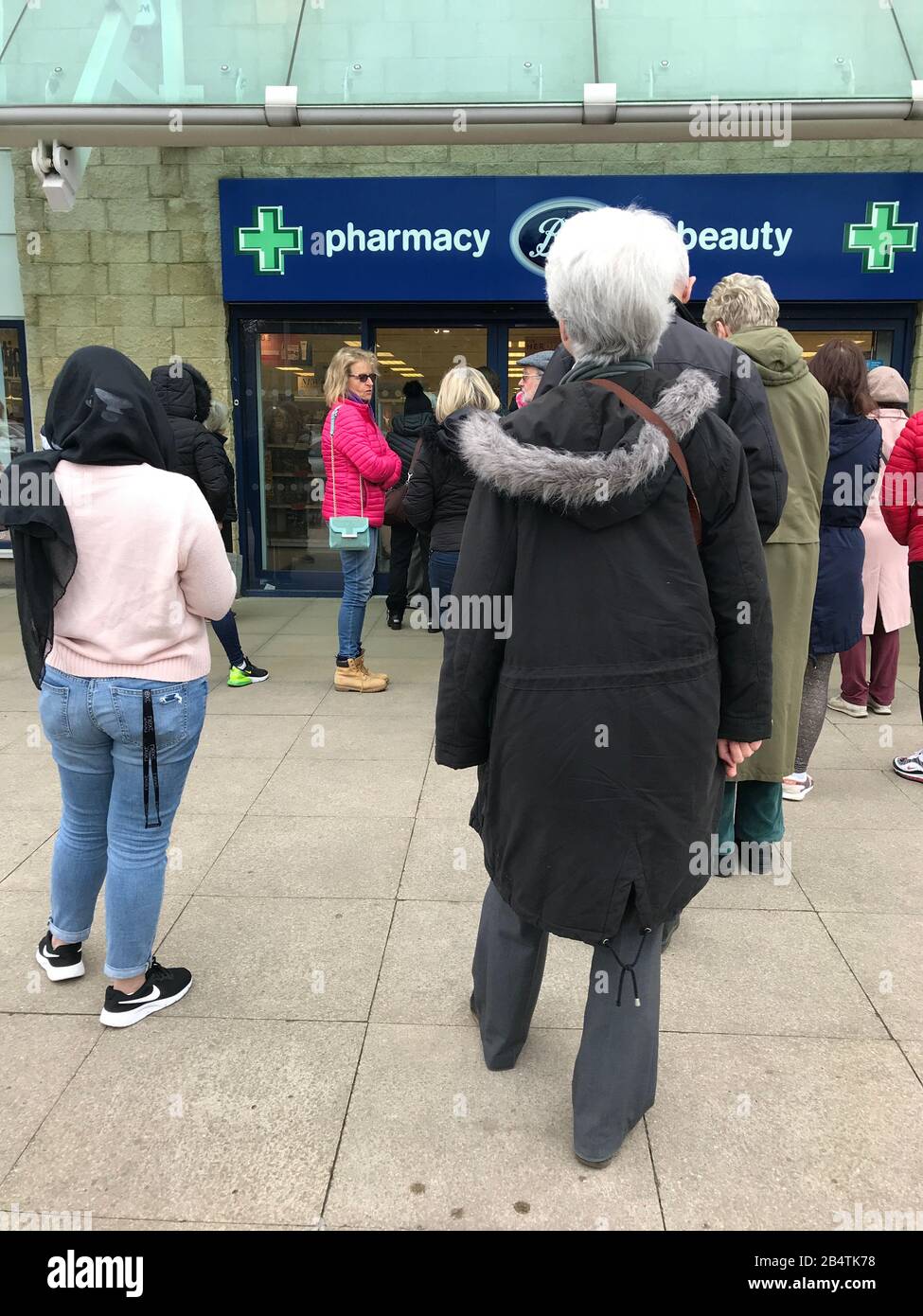 People queue outside a Boots pharmacy store in west London where stocks of hand sanitiser are limited to two per person. Stock Photo