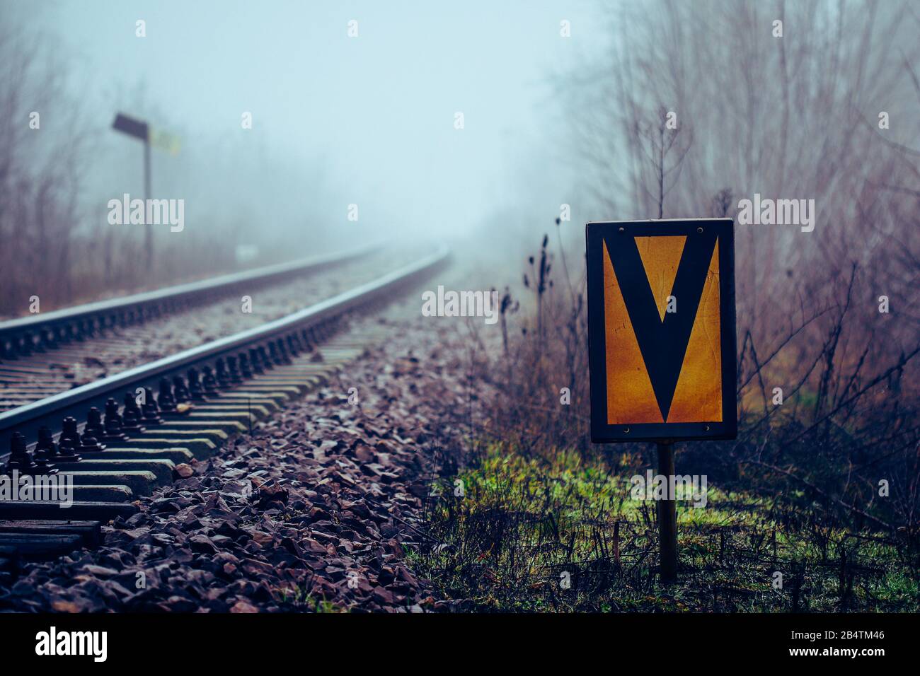 Railway sign meaning beginning of speed limit stretch at railroad  embankment with rail track disappearing in mist in background Stock Photo -  Alamy