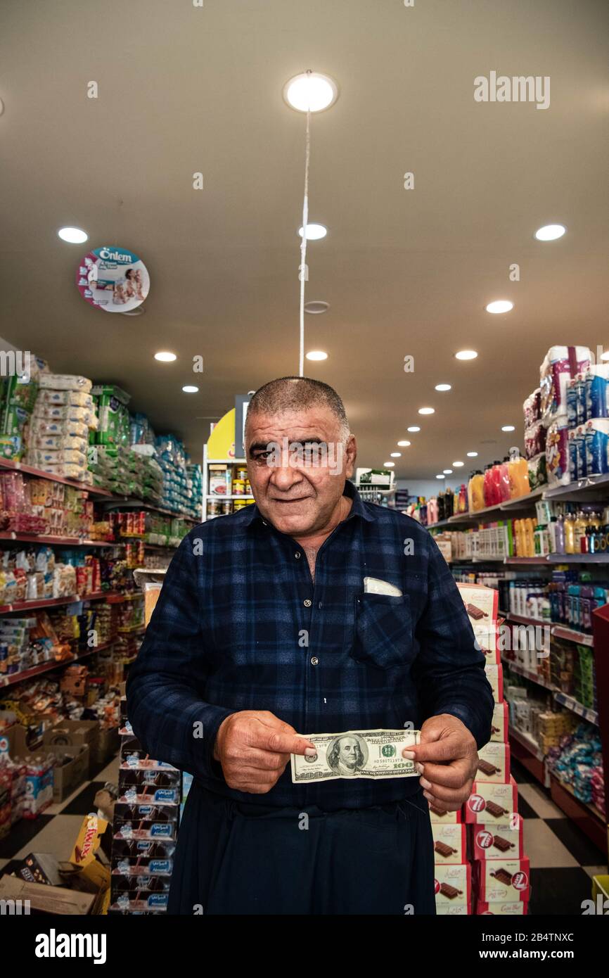 Iraq, Iraqi Kurdistan, Arbil, Erbil. Portait of a iraqi kurdish man in a store. He is holding a dollar bill. Stock Photo
