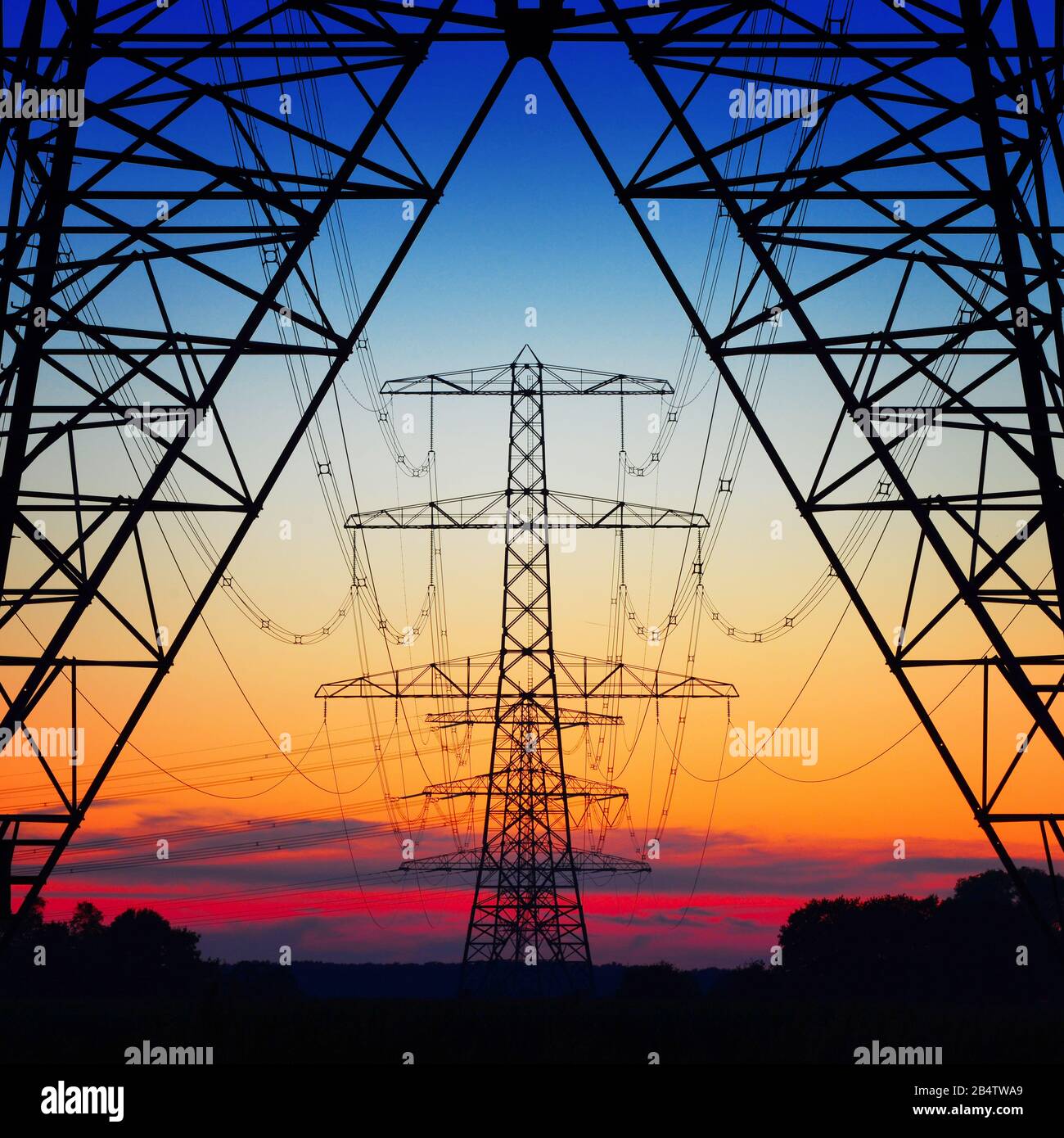 symmetric view of power pylons against a beautiful coloured evening sky Stock Photo