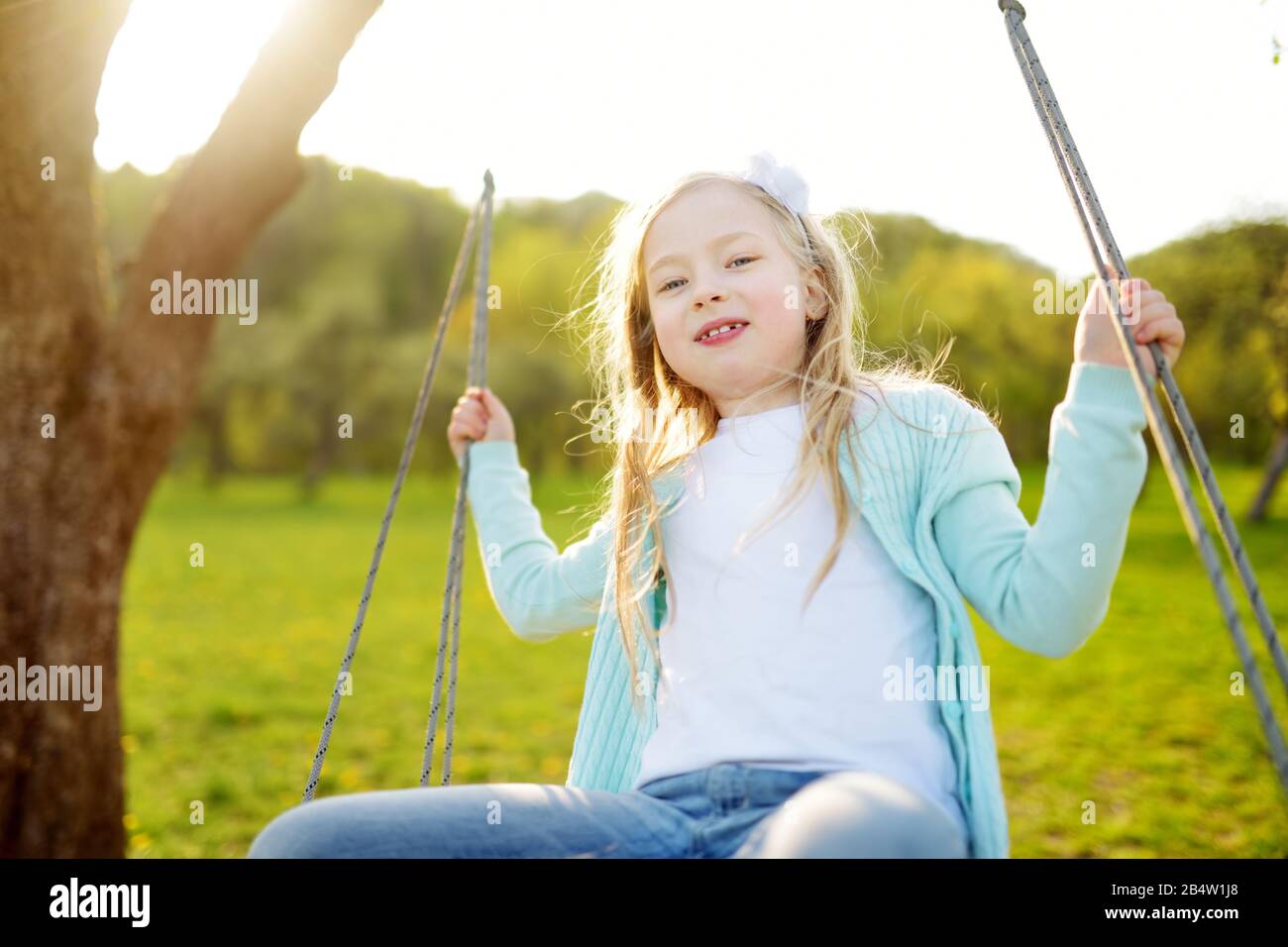 Cute little girl having fun on a swing outdoors in summer garden. Summer leisure for small kids. Stock Photo