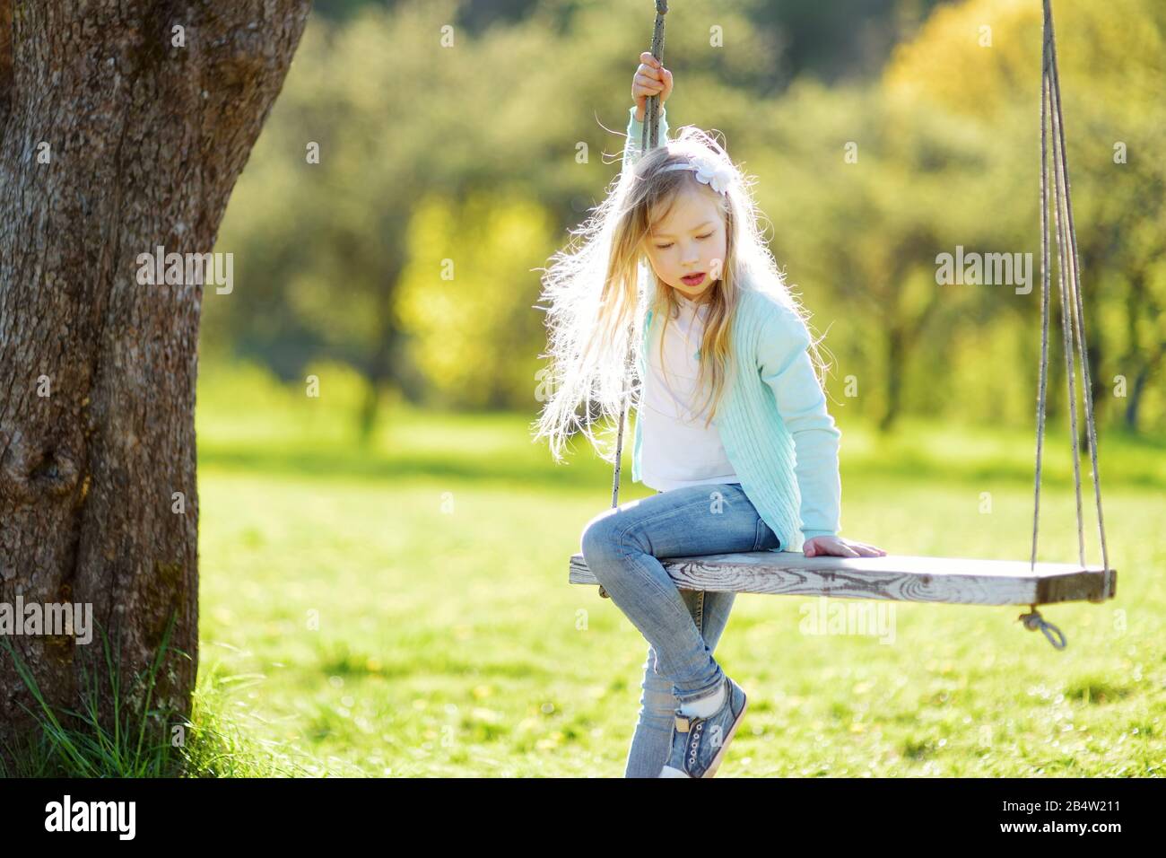 Cute little girl having fun on a swing outdoors in summer garden. Summer leisure for small kids. Stock Photo