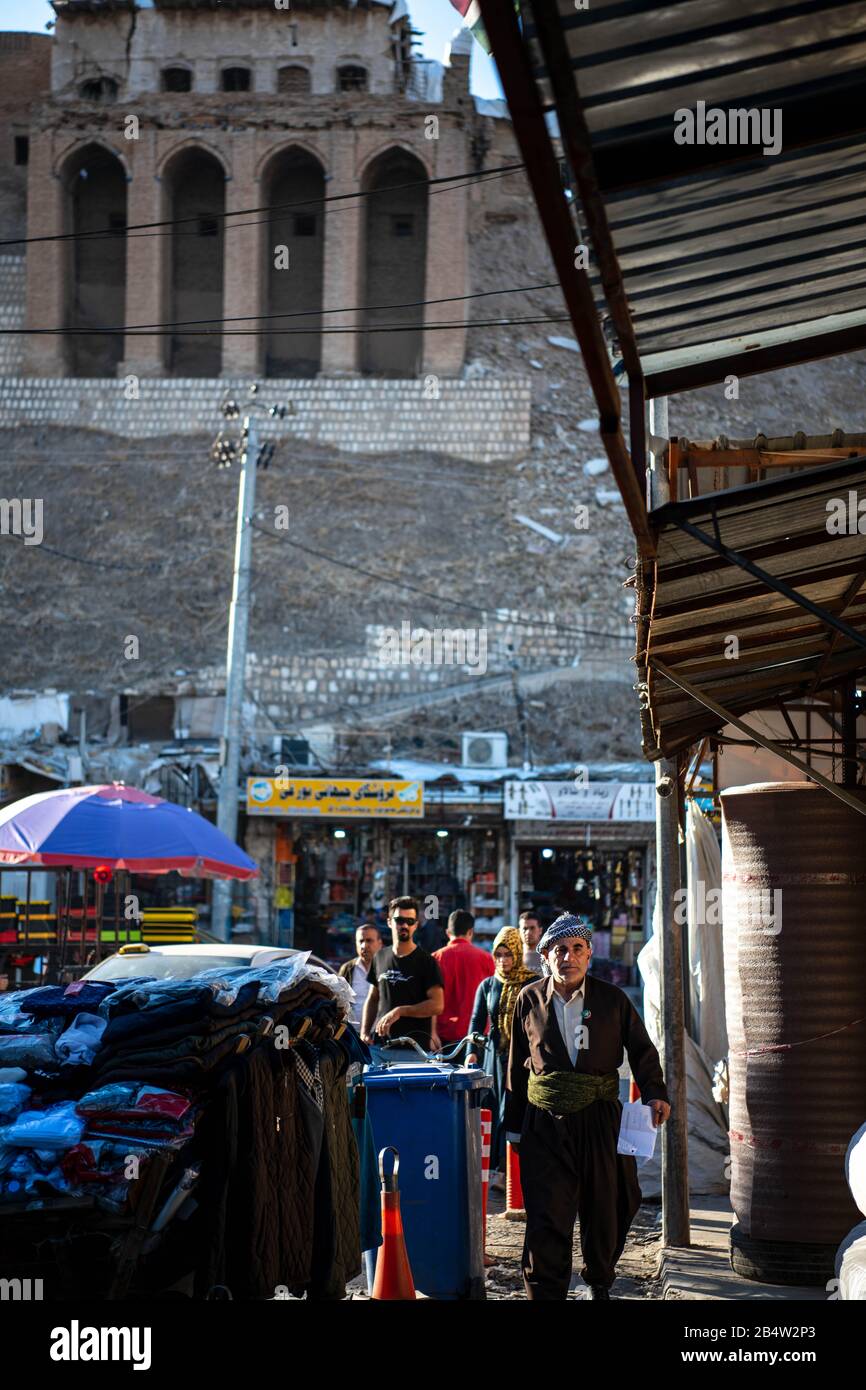 Iraq, Iraqi Kurdistan, Arbil, Erbil. a man walks next to markets. In the background stands Erbil Qalat citadel Stock Photo