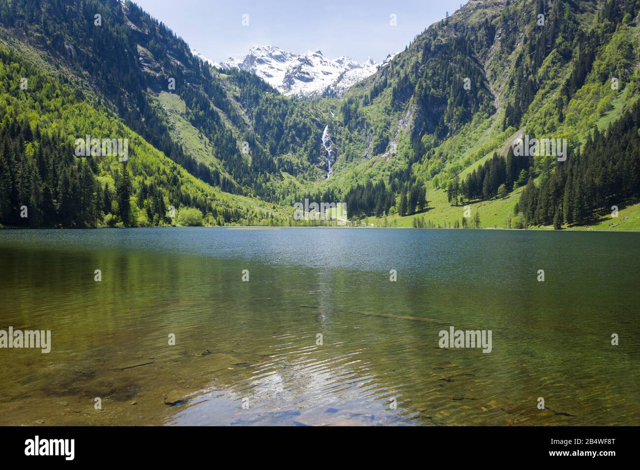 Enchanting alpine valley with mountain lake and waterfall in the background Stock Photo