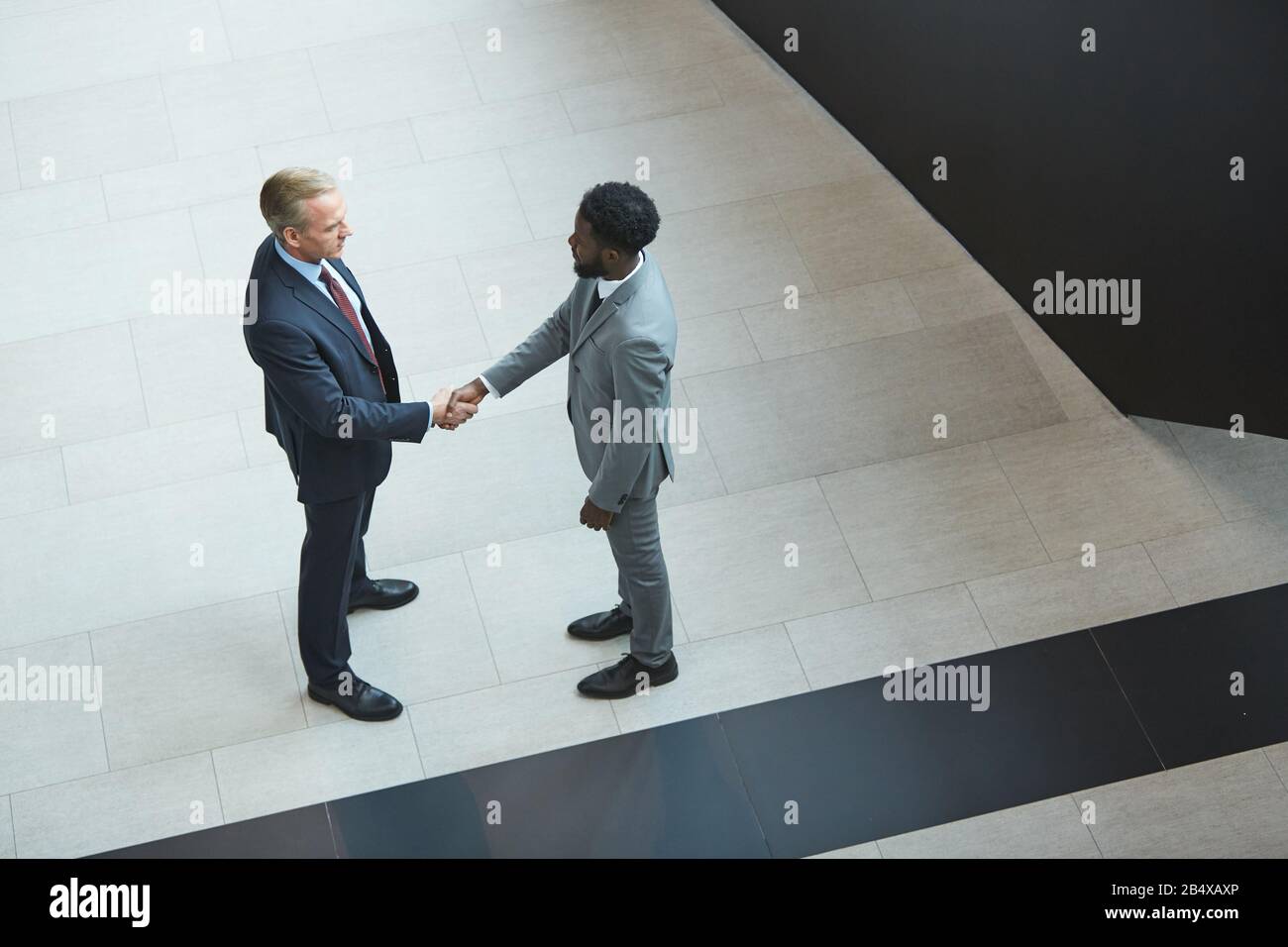 Horizontal high angle shot of two modern men wearing suits standing in front of each other shaking hands Stock Photo