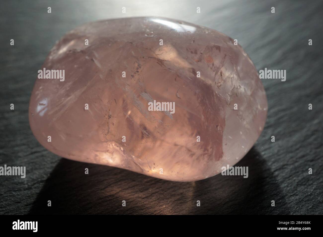 Rose quartz tumbled pebble on gray slate background, against the light Stock Photo