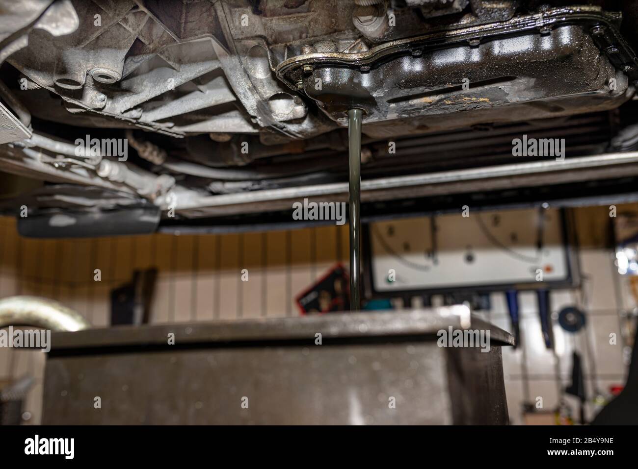 Draining used diesel engine oil from an oil pan into a metal container in a car workshop. Stock Photo