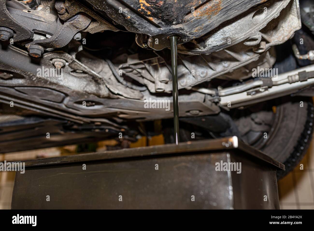 Draining used diesel engine oil from an oil pan into a metal container in a car workshop. Stock Photo