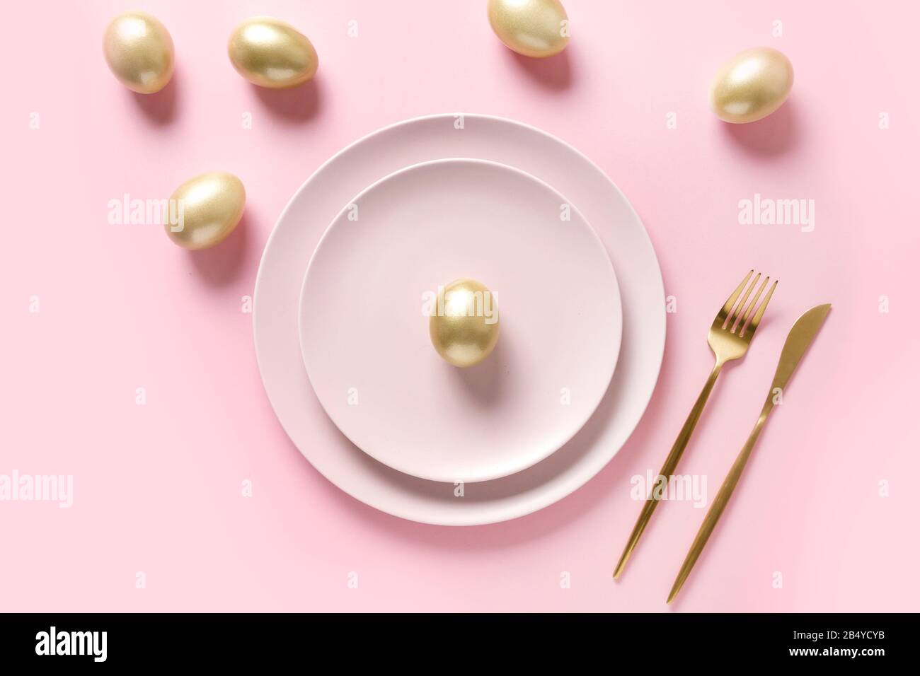 Easter table setting decorated golden eggs on pink table. Elegance dinner. Top view. Stock Photo