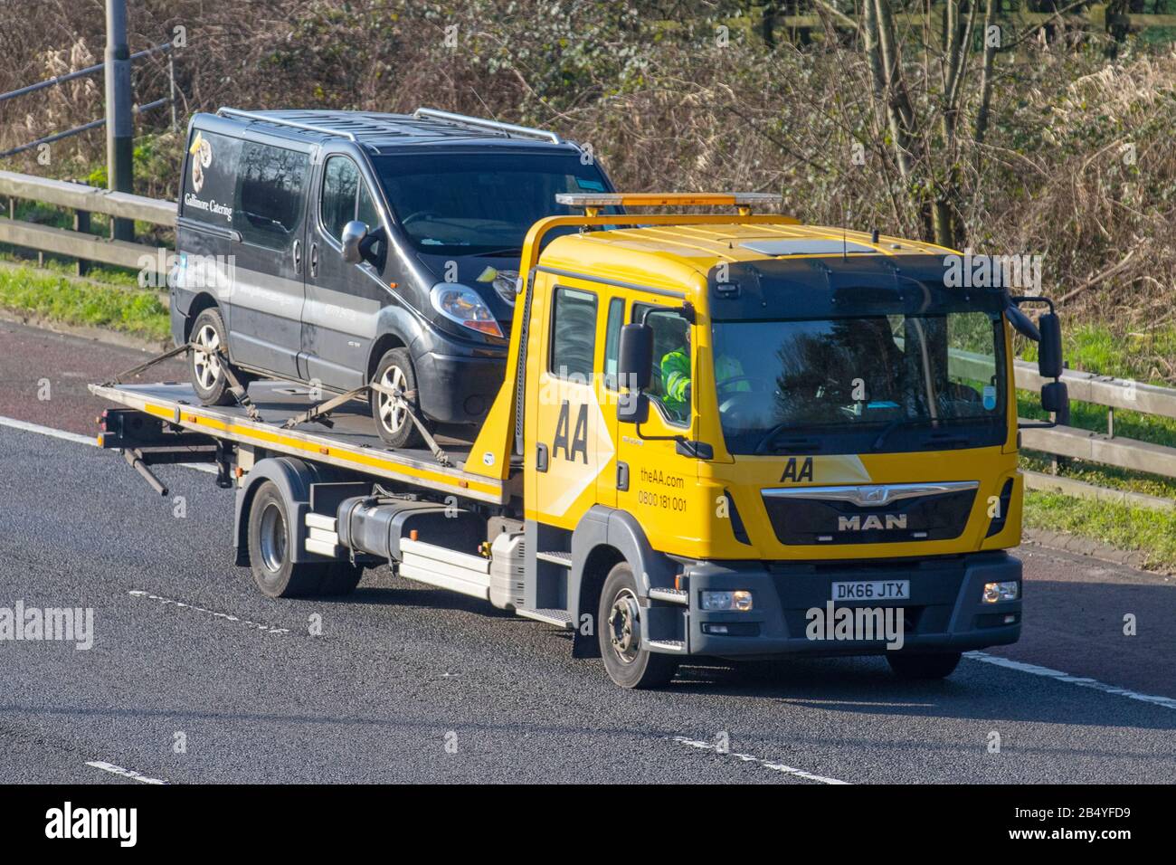 AA Van recovery truck carrying broken down van; Side view of rescue breakdown recovery lorry truck transporter transporting unmarked black van driving along  M6, Lancaster, UK; Vehicular traffic, transport, modern, north-bound on the 3 lane highway. Stock Photo