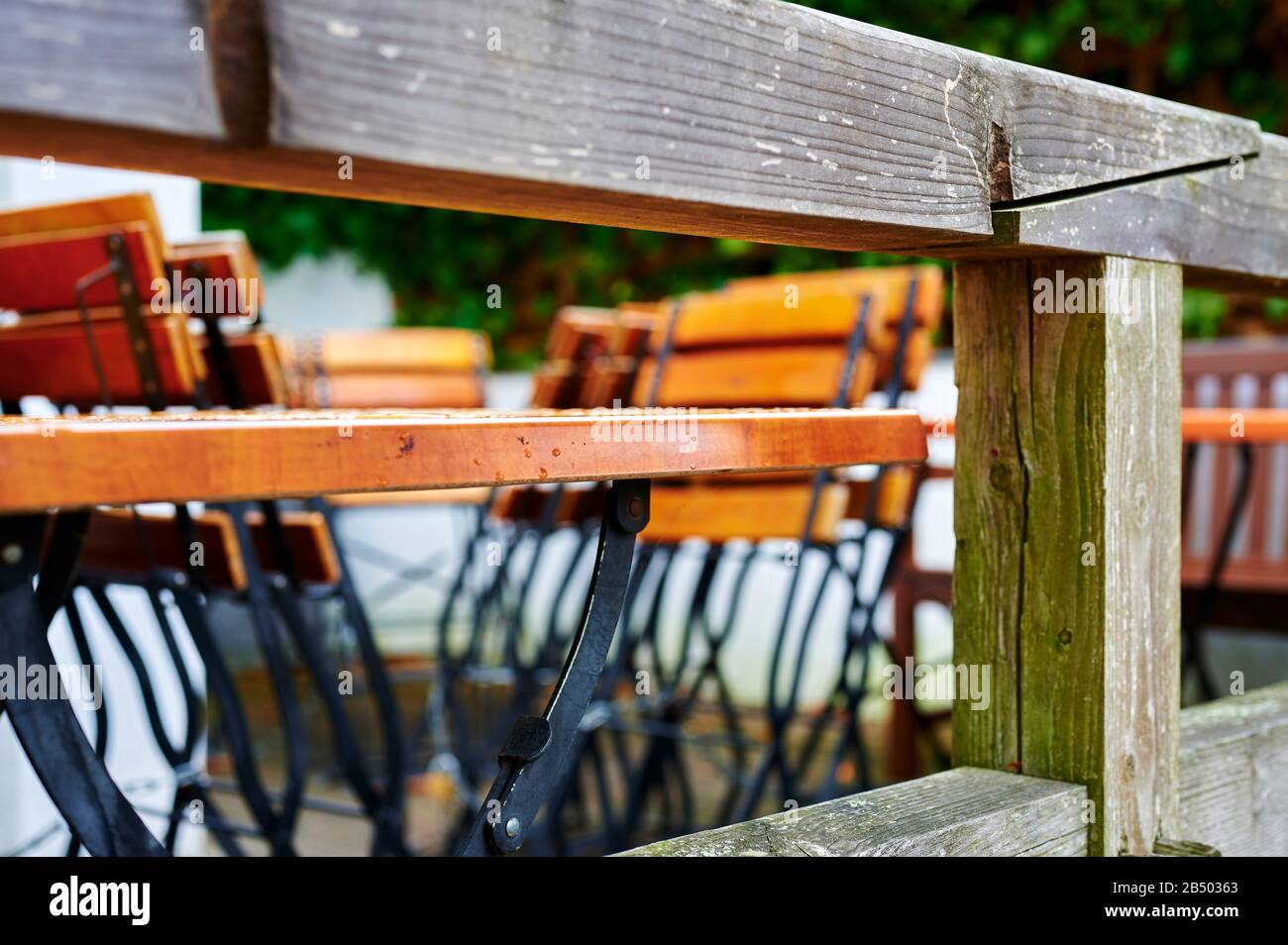 Looking through a wooden terrace railing to tables and folded chairs of a restaurant in bad weather. Stock Photo
