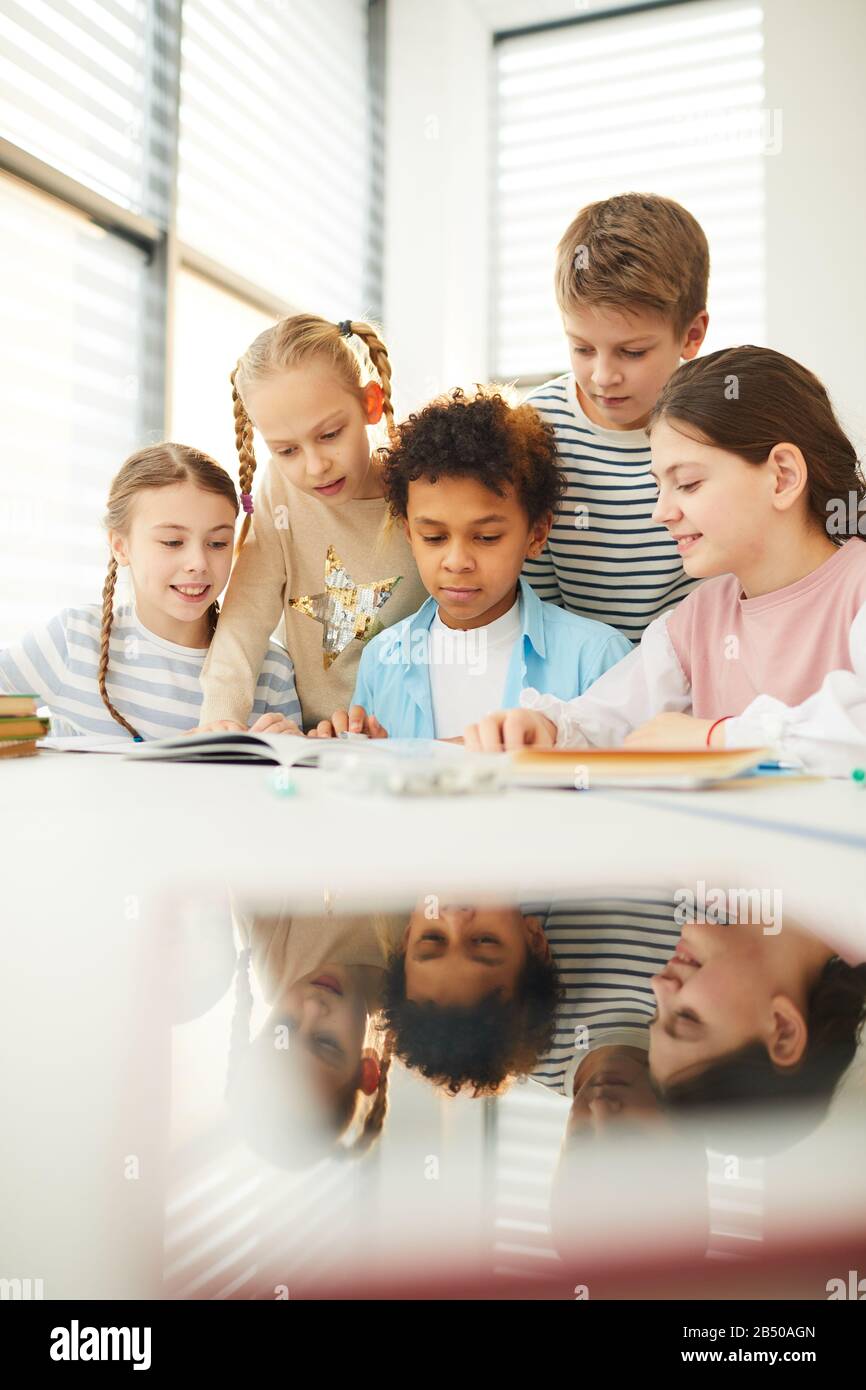 Group of modern classmates helping their good friend with homework task he couldn't do, vertical shot Stock Photo