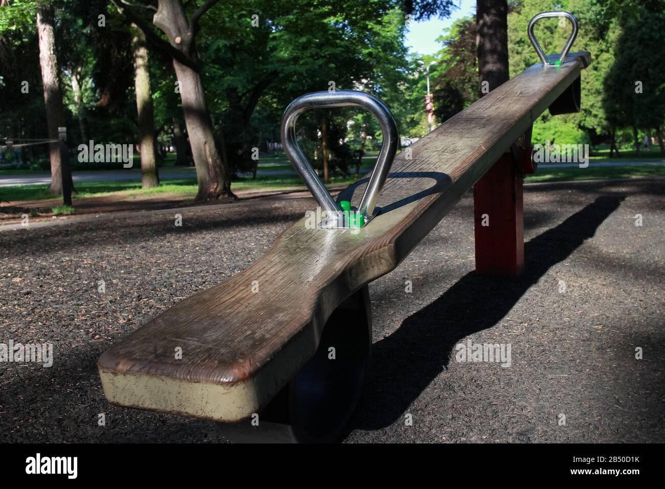 wooden seesaw for two with metal handles on an empty playground in a summer park, image on the topic of child protection, abducted or missing children Stock Photo