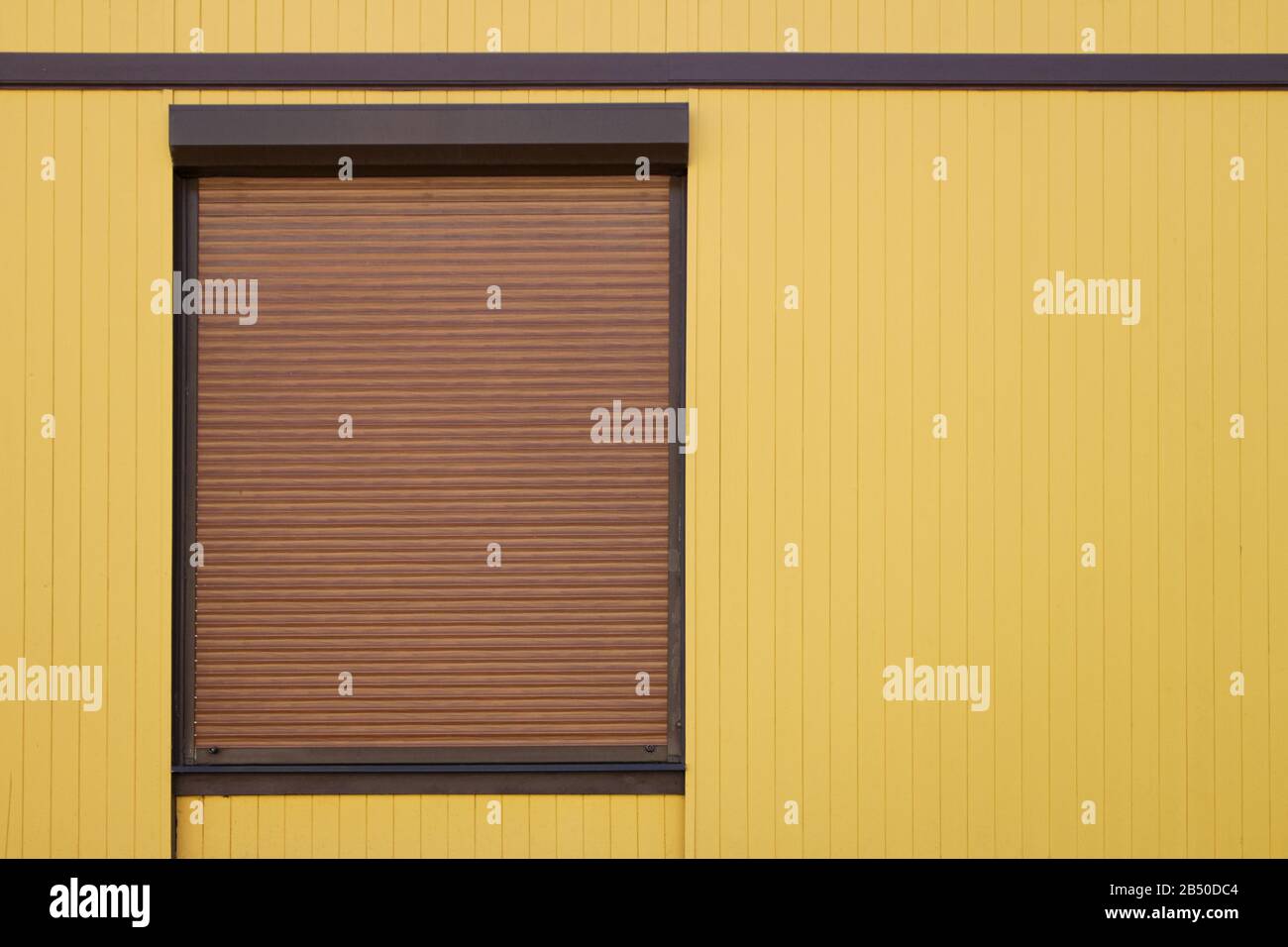 window with a brown steel protective roller shutter on a yellow building facade, background for design and copy space for text Stock Photo