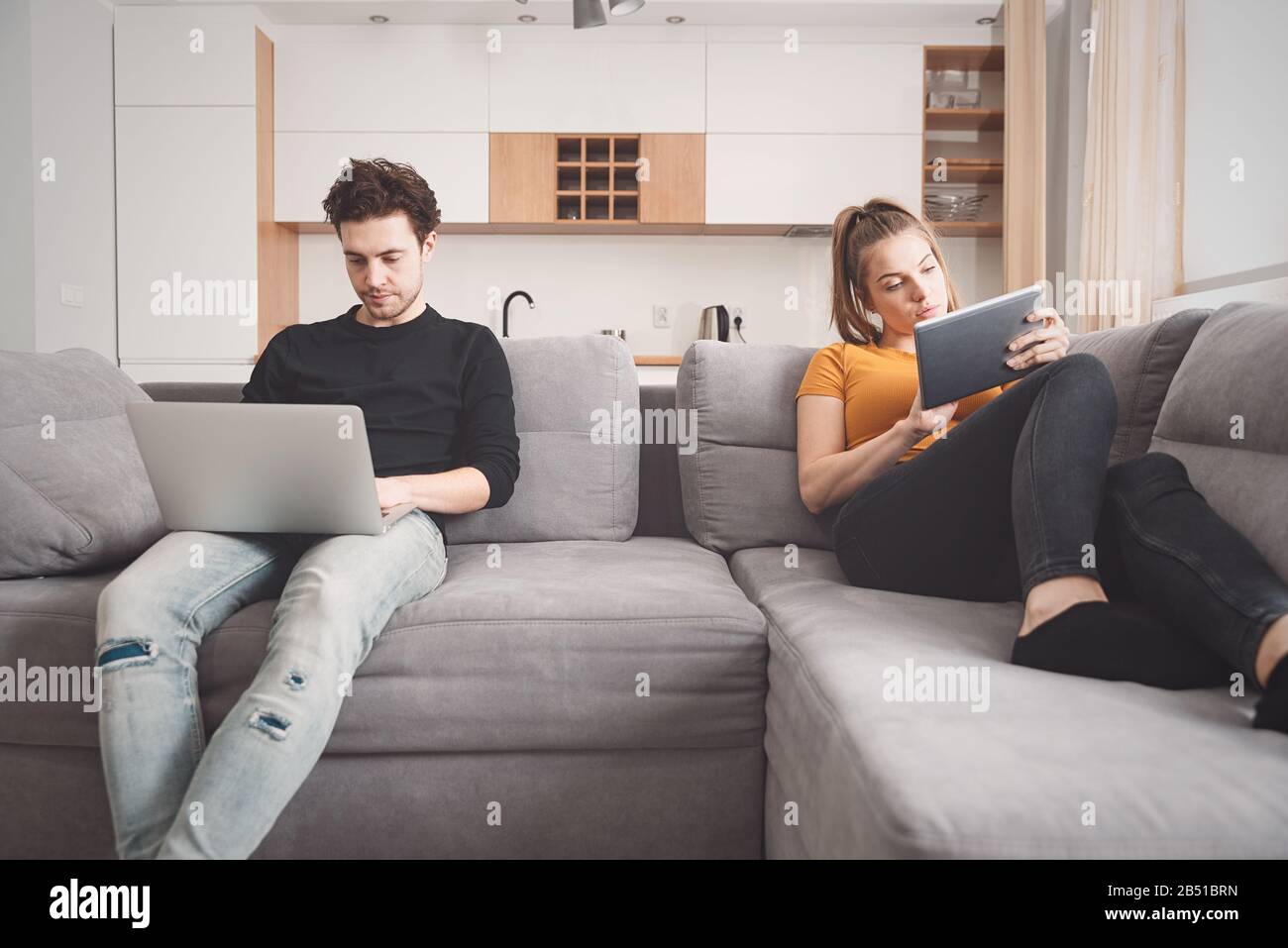 Crisis in a partnership, separation, internet addiction. Couple separated on sofa in living room Stock Photo