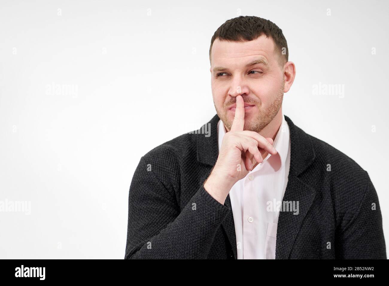 Man saying hush and be quiet with finger on lips gesture looking at camera Stock Photo