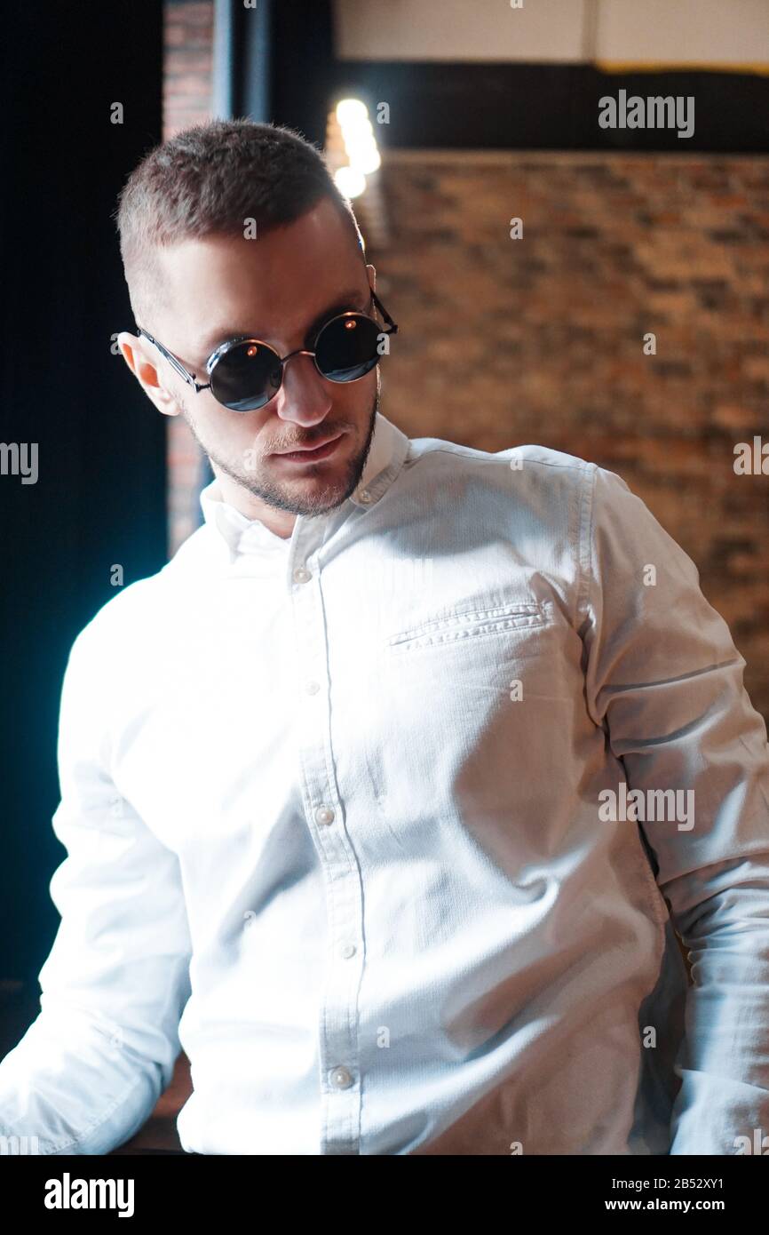 Handsome young man wearing vintage round black glasses looking forward near red brick wall Stock Photo