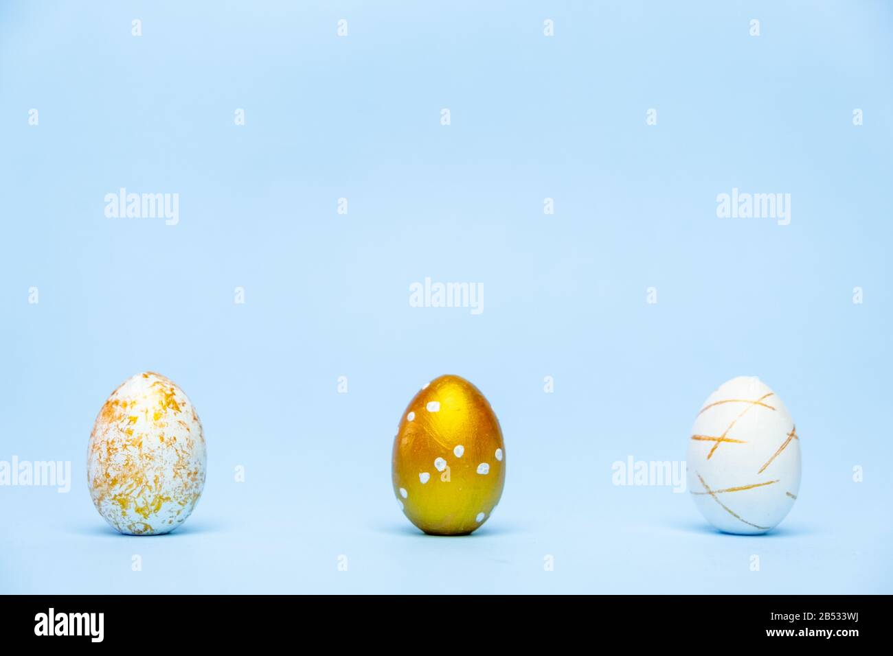 Three easter trendy golden decorated eggs on blue background. Happy Easter card with copy space for text Minimal easter style Stock Photo