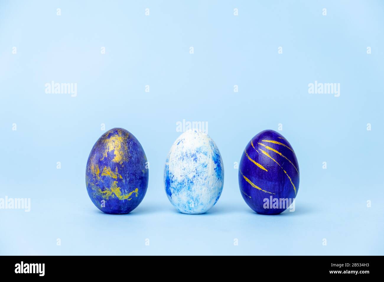 Three easter trendy colored classic blue, white and golden decorated eggs on blue. Happy Easter card with copy space for text. Minimal style. Stock Photo