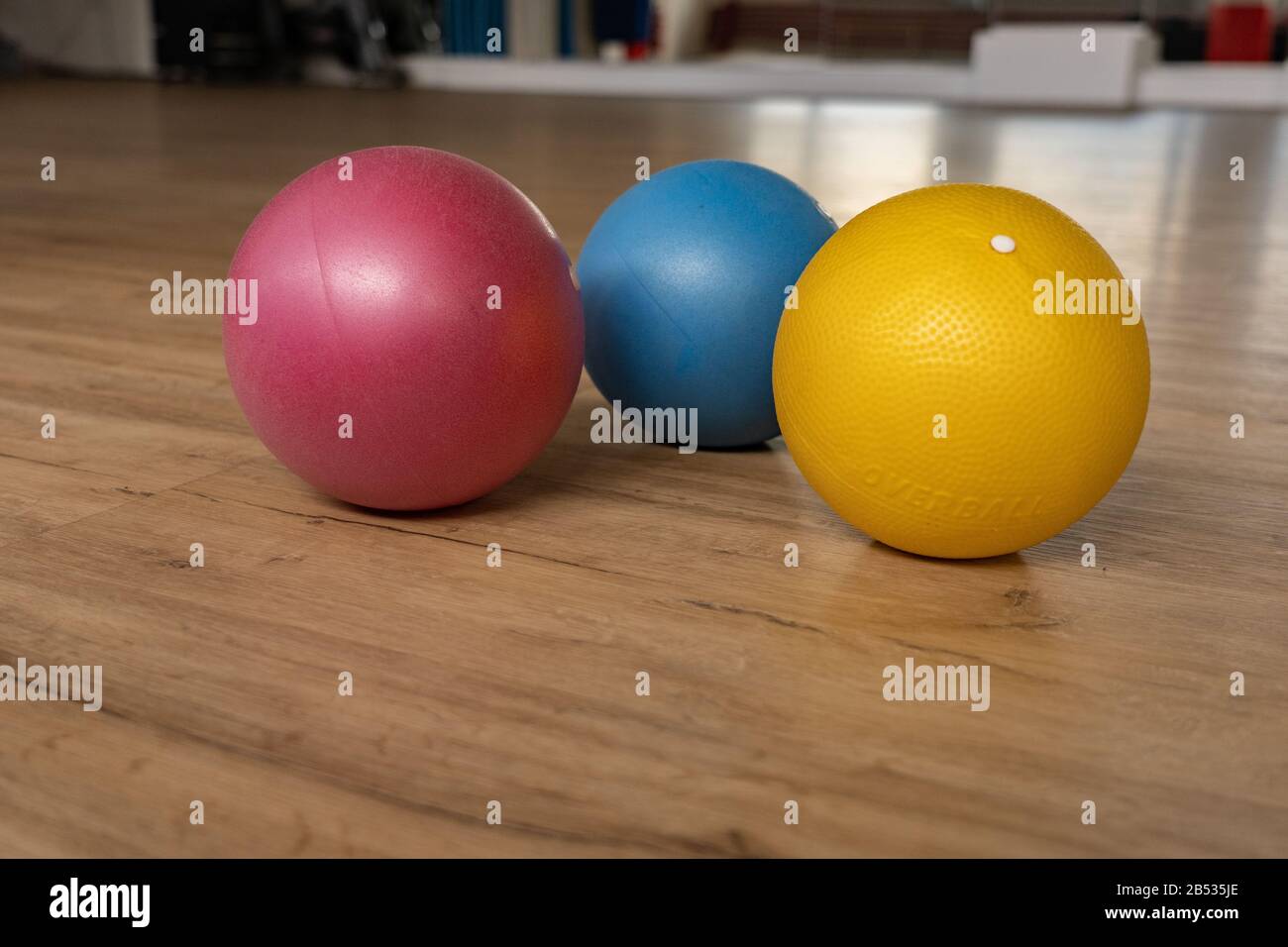 Three small and colorful gymnastic balls on wooden floor of a gymnastic hall of a group fitness center. Reflections of mirror in background. Low angle Stock Photo