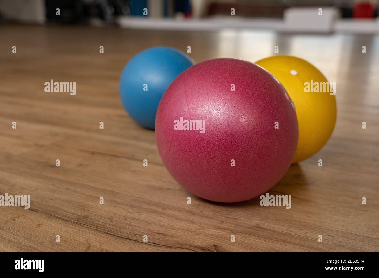 Three small and colorful gymnastic balls on wooden floor of a gymnastic hall of a group fitness center. Reflections of mirror in background. Low angle Stock Photo