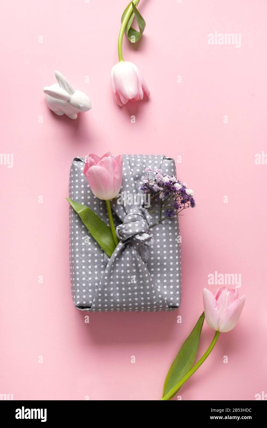 Spring eco-friendly gift wrapped in grey textile with tulip flowers decor on pink. Sustainable gift. Zero waste. Easter holiday. Traditional Japanese Stock Photo