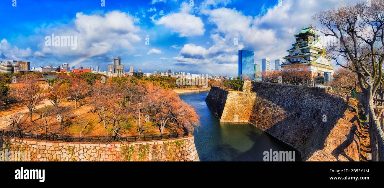 Rainbow over Osaka city in Japan with local garden, historic park surrounded by stone walls, water moat and traditional tower. Stock Photo