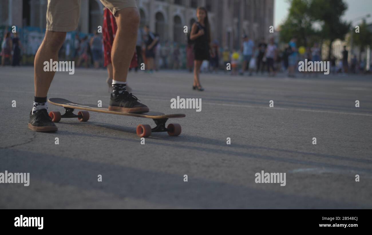 The legs of a light-skinned skateboarder in shorts stopped in the center of a crowded European city street. Stock Photo
