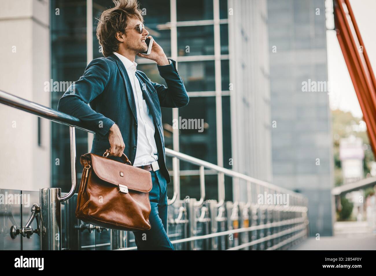 Young man in a sute standing outdoors and talking on the mobile phone and smiling Stock Photo