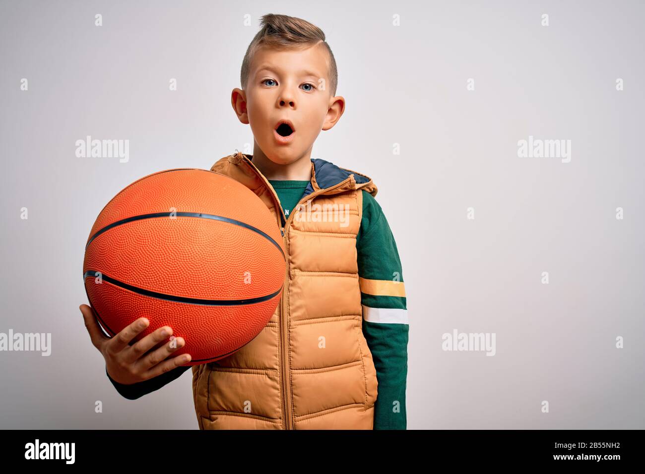 Young little caucasian sports kid playing basketball holding orange