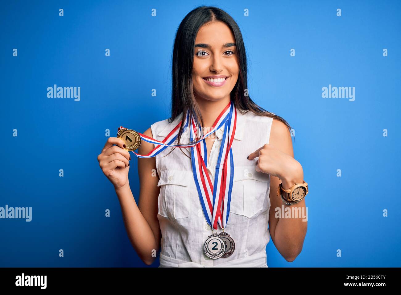 Young beautiful brunette atthete champion woman winning medals over blue  background with surprise face pointing finger to himself Stock Photo - Alamy