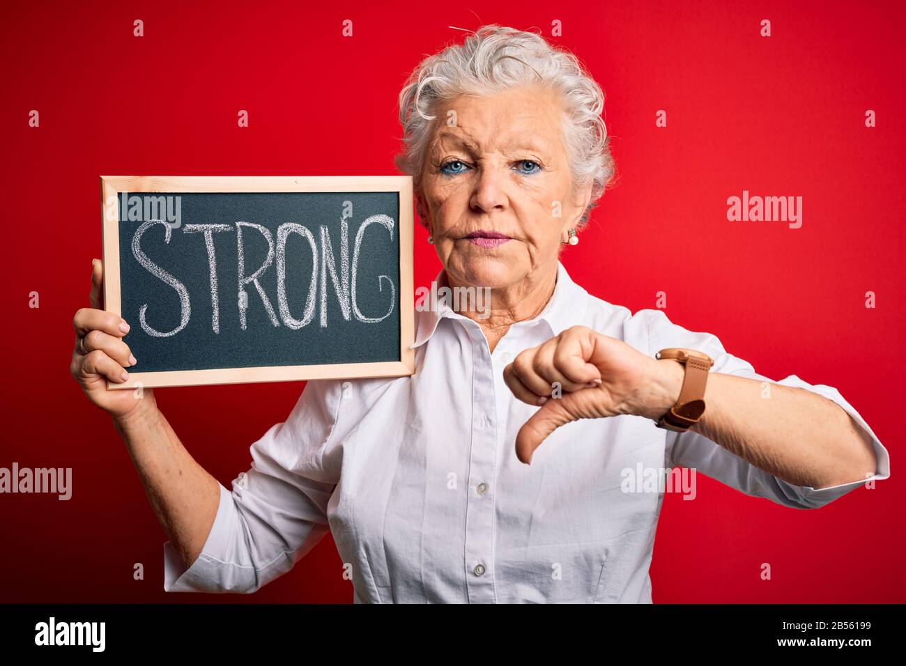 Senior beautiful woman holding blackboard with strong message over ...