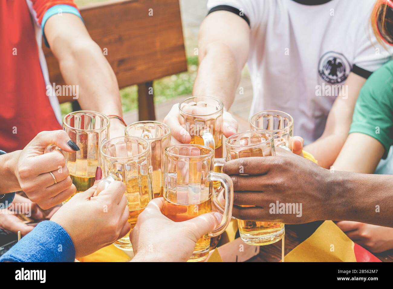 Multination football supporters cheering with beers in pub outdoor before soccer match - Happy sport fans having fun together drinking together - Bond Stock Photo