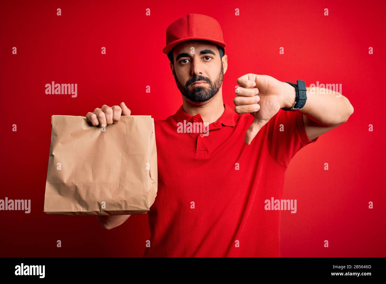 Young handsome delivery man with beard wearing cap holding takeaway ...