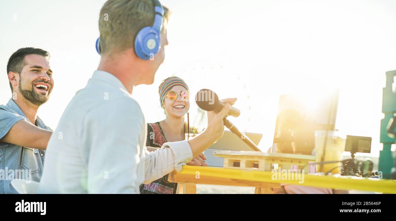 Happy young people making a video live streaming from beach party at sunset - Man vlogger recording video feed on the beach at sunset - Focus on left Stock Photo