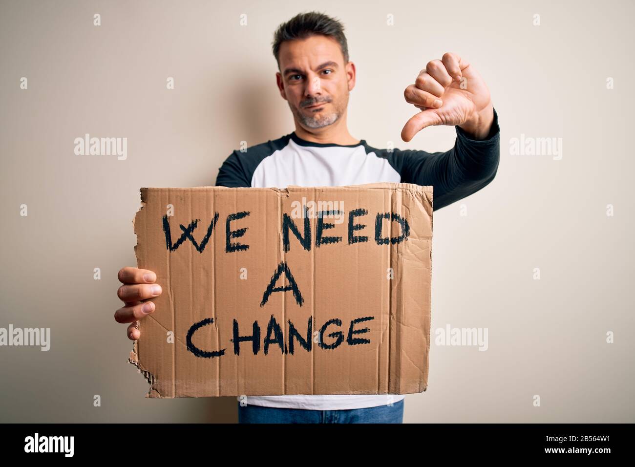 Young handsome activist man holding banner with change message over pink background with angry face, negative sign showing dislike with thumbs down, r Stock Photo