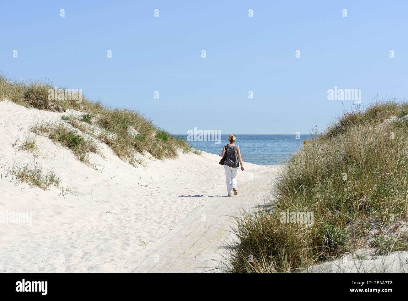 A woman walking to a beach with the sea in the background, Sandhammaren, Ystad, Skane, Sweden Stock Photo