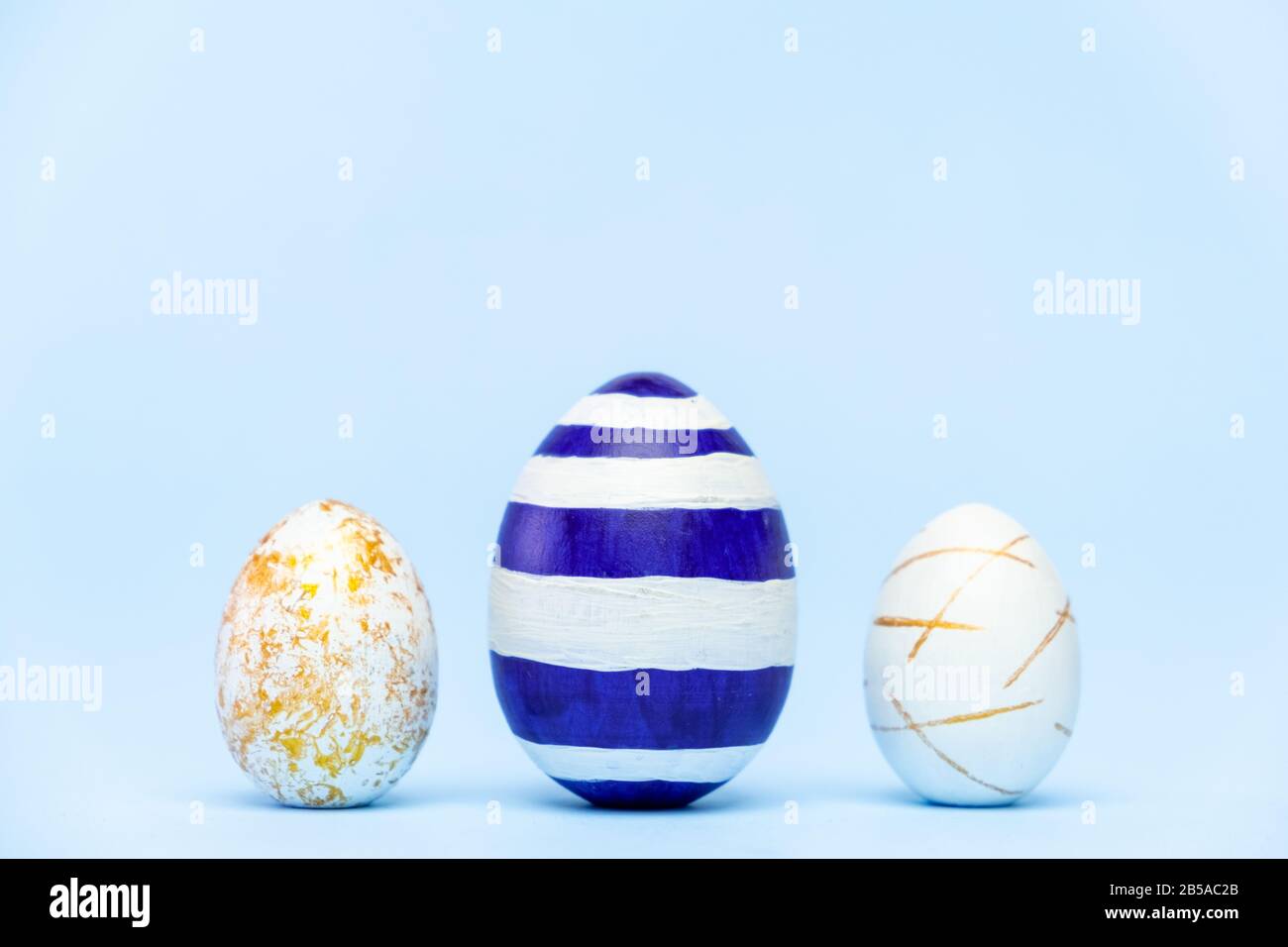Three easter trendy colored classic blue and golden decorated eggs on blue background. Happy Easter card with copy space for text Minimal easter style Stock Photo