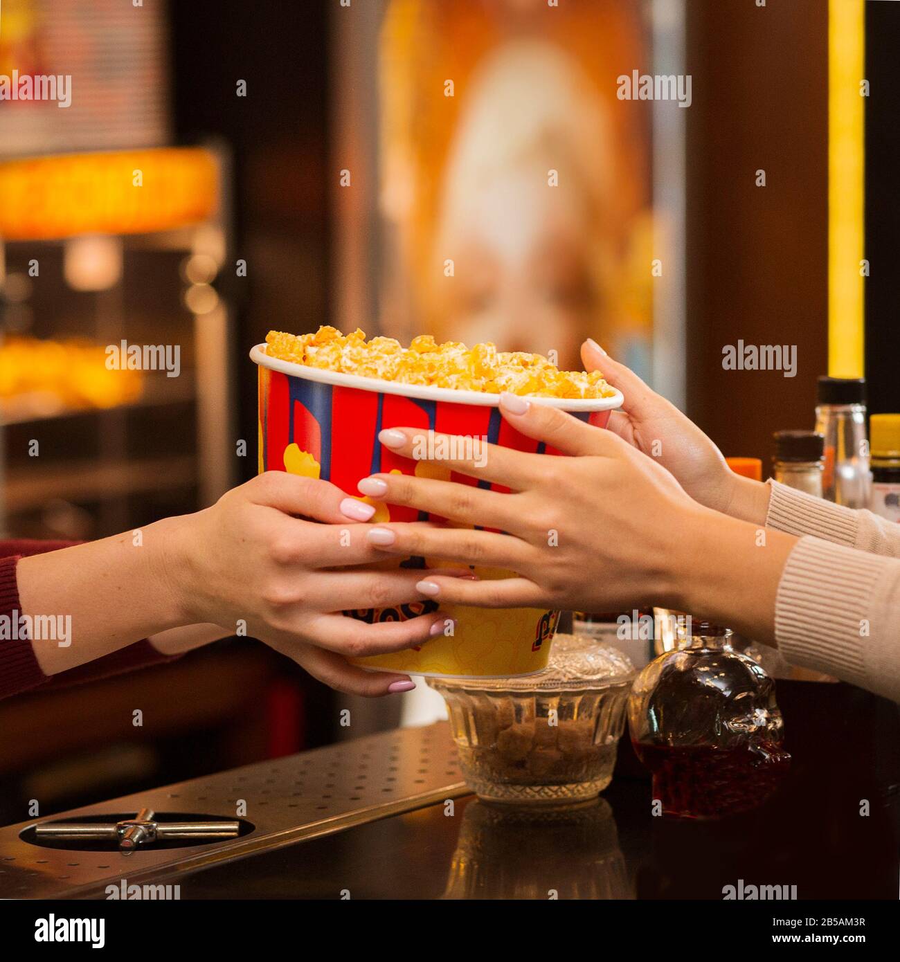 Young woman buying popcorn from employee in cinema lobby, closeup Stock Photo