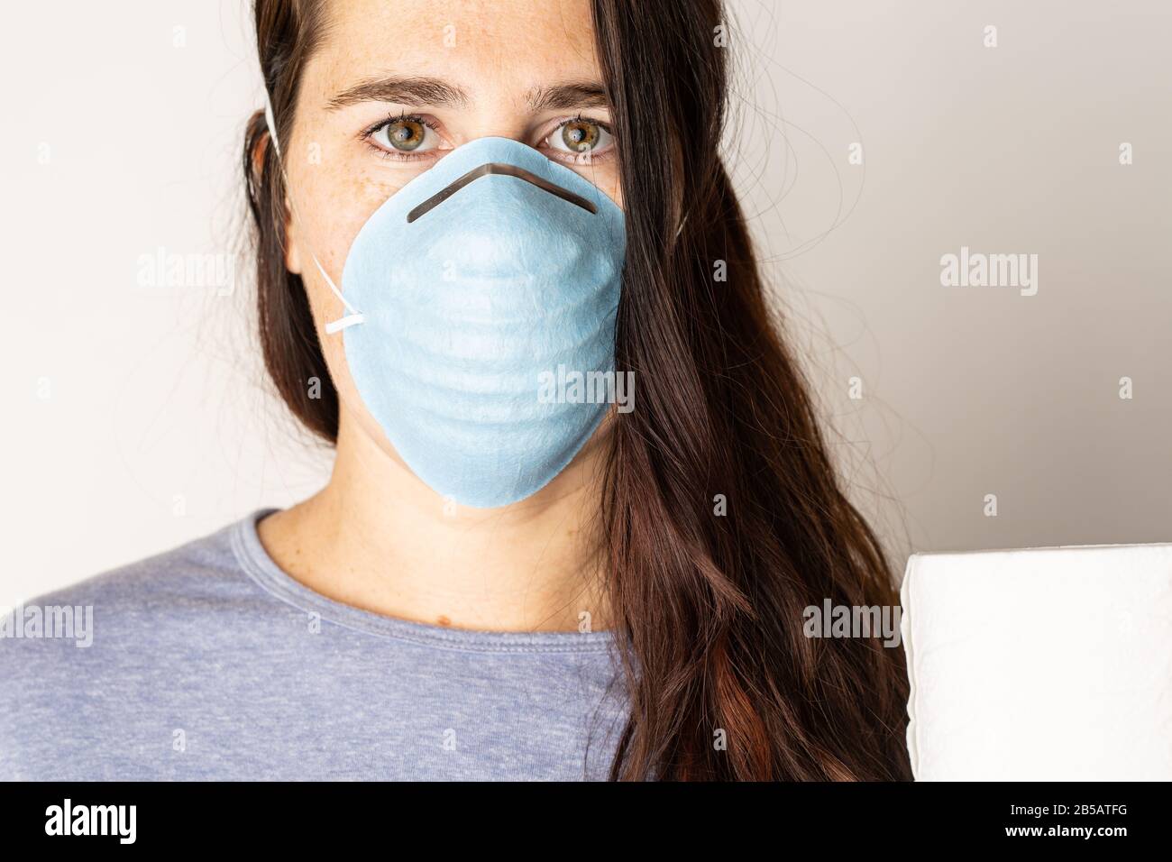 A woman is wearing a face mask for protection from the Corona Virus and has stocked up on her toilet paper stash in case of quarantine. Stock Photo