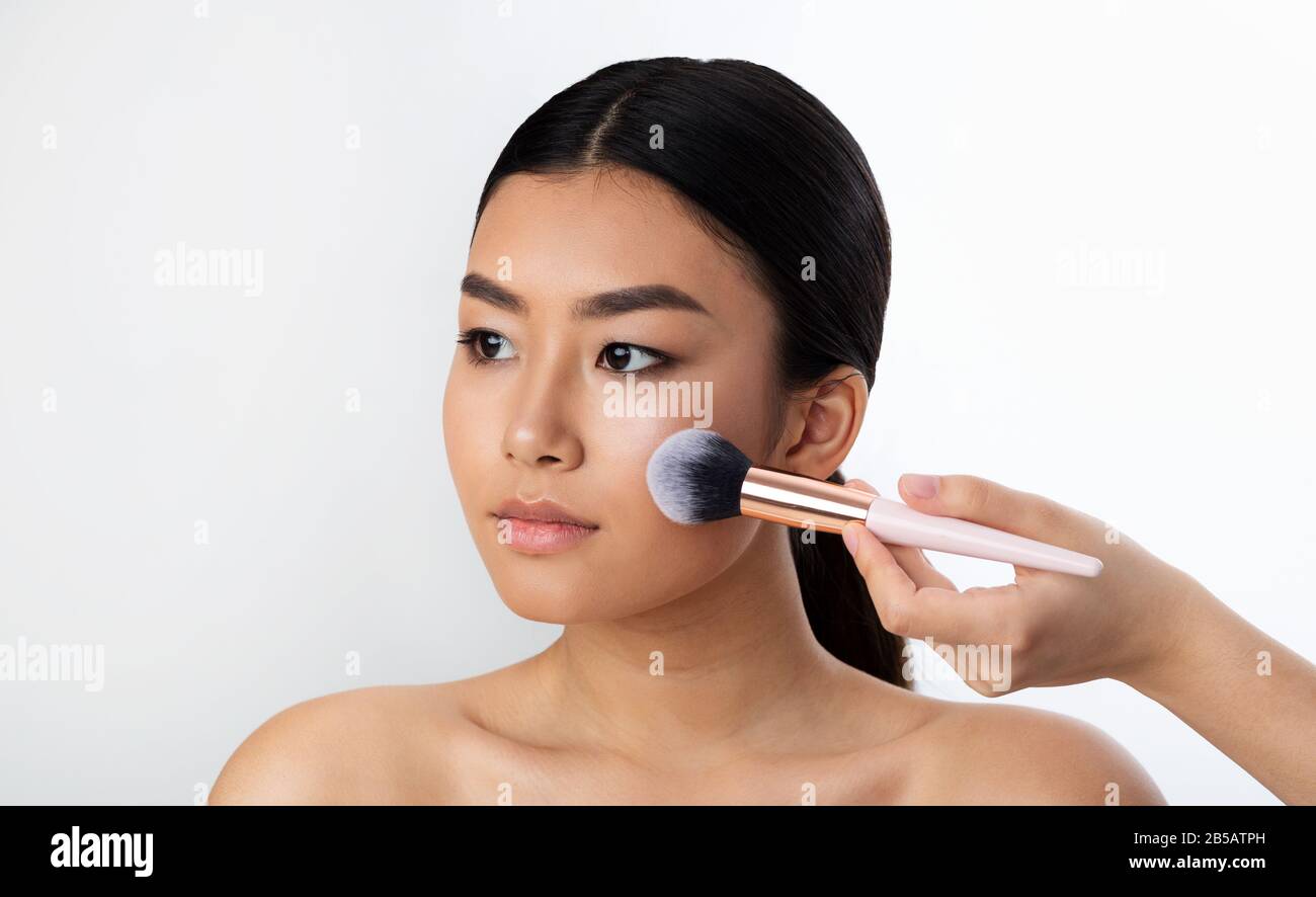 Chinese Girl Using Brush Applying Face Powder On White Background Stock Photo