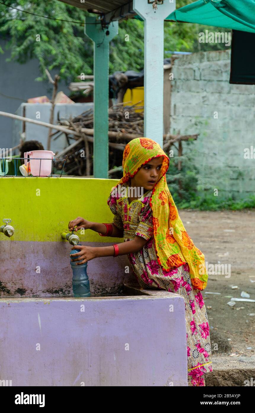 Young little girl filling water in bottle from tap somewhere in Kutch, Gujarat, India Stock Photo