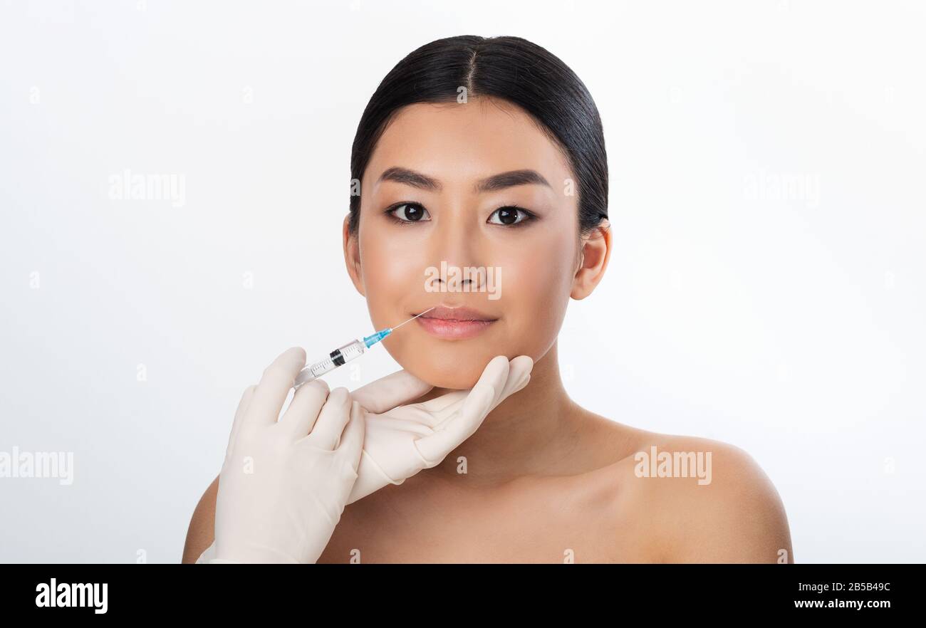 Korean Girl Receiving Injection During Lips Plumping Procedure, White Background Stock Photo
