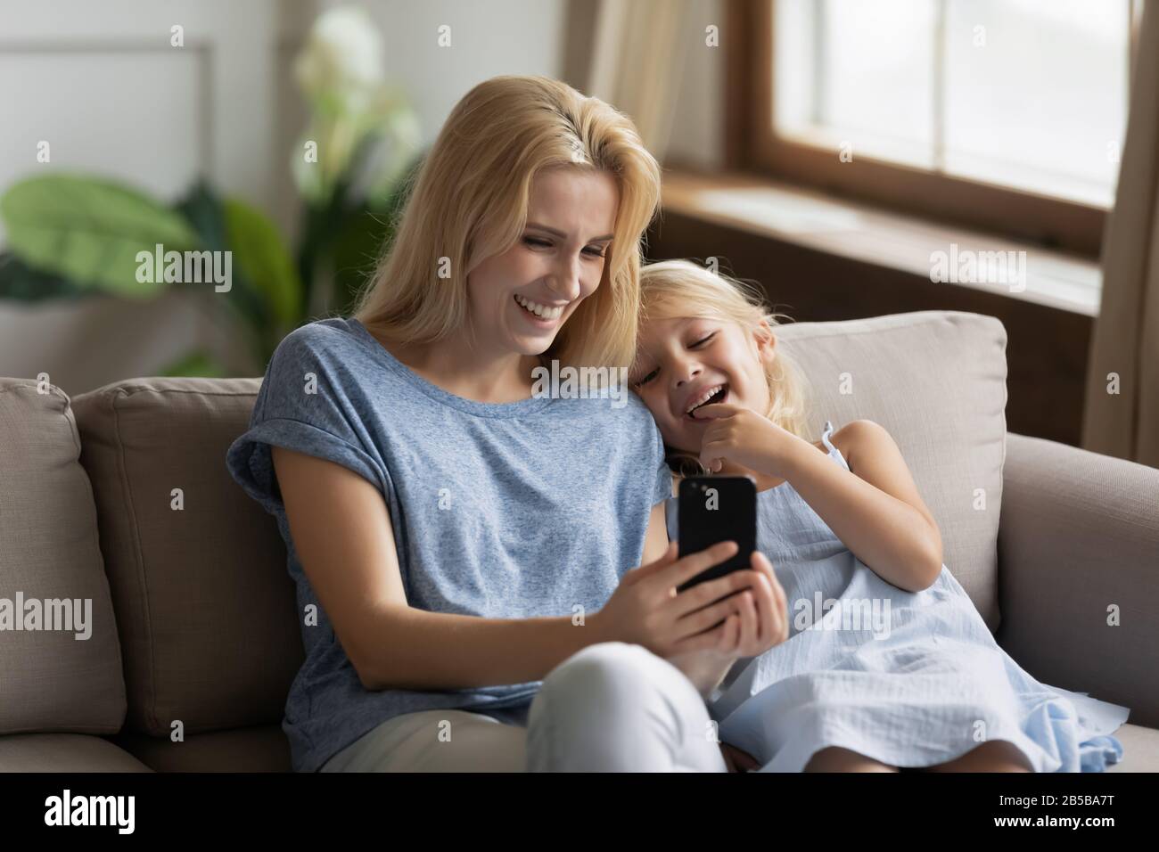 Overjoyed young mum and little daughter using cellphone Stock Photo - Alamy