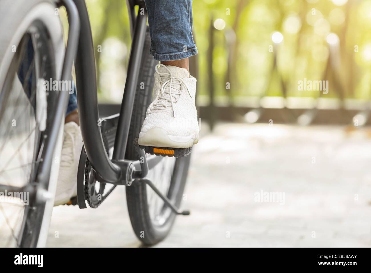 Feet On Pedals Of Unrecognizable Black Man Riding Bicycle In Park Stock Photo