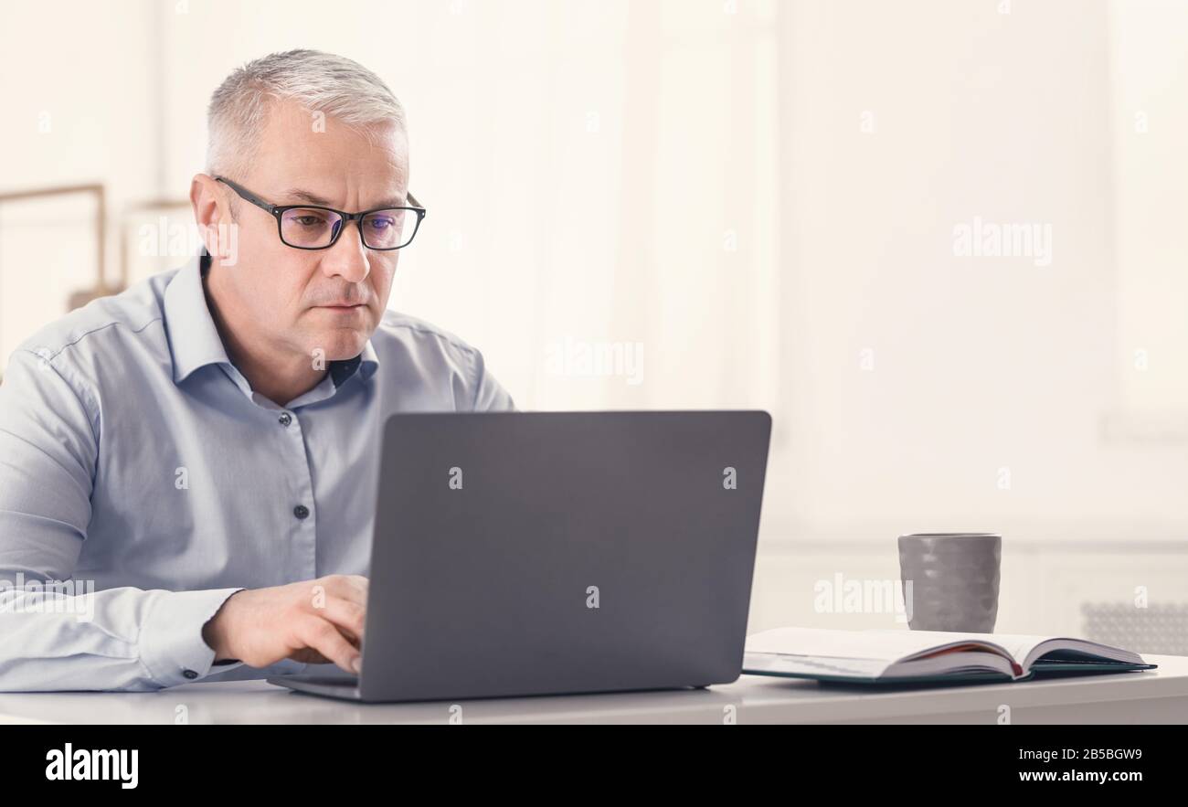 Serious senior man using laptop at home Stock Photo