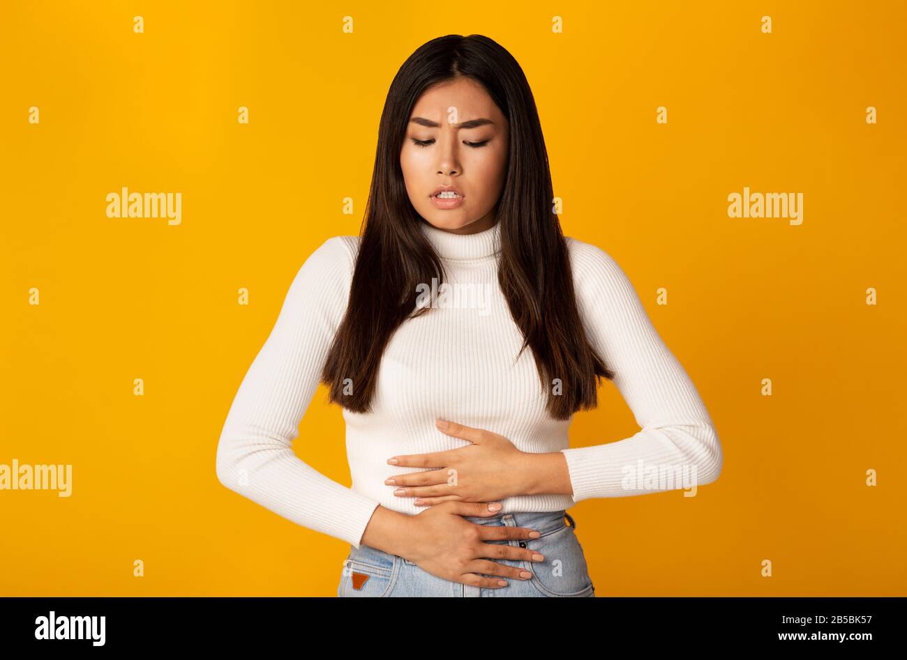 Asian Girl Touching Stomach Standing On Yellow Background Stock Photo