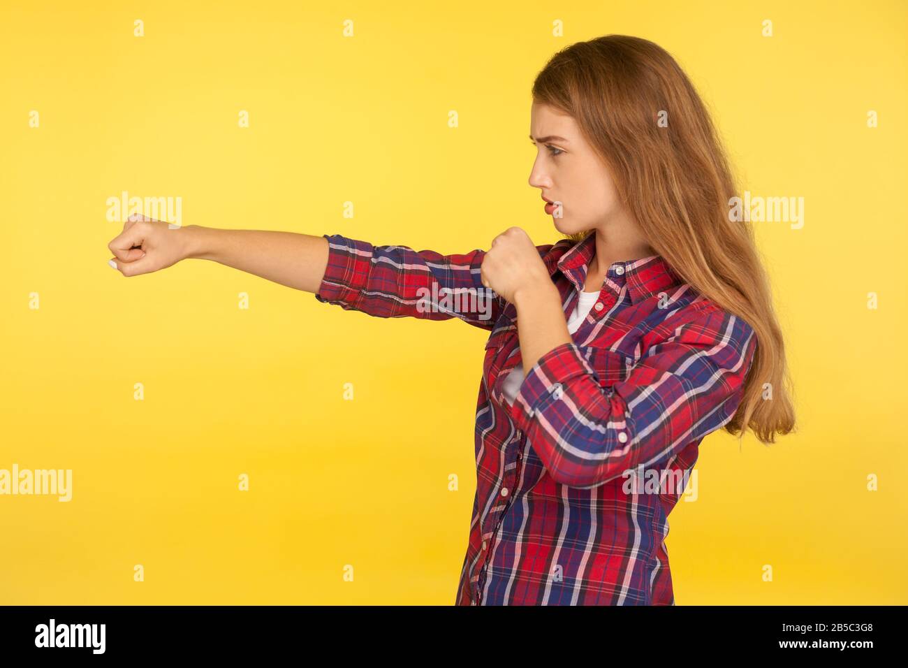 Profile of strong and determined ginger girl in checkered shirt punching air with fist and looking self-confident, female struggle, fighting spirit. i Stock Photo
