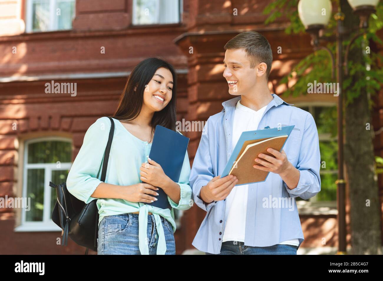 Cheerful university friends resting between classes outdoors, chatting and smiling Stock Photo
