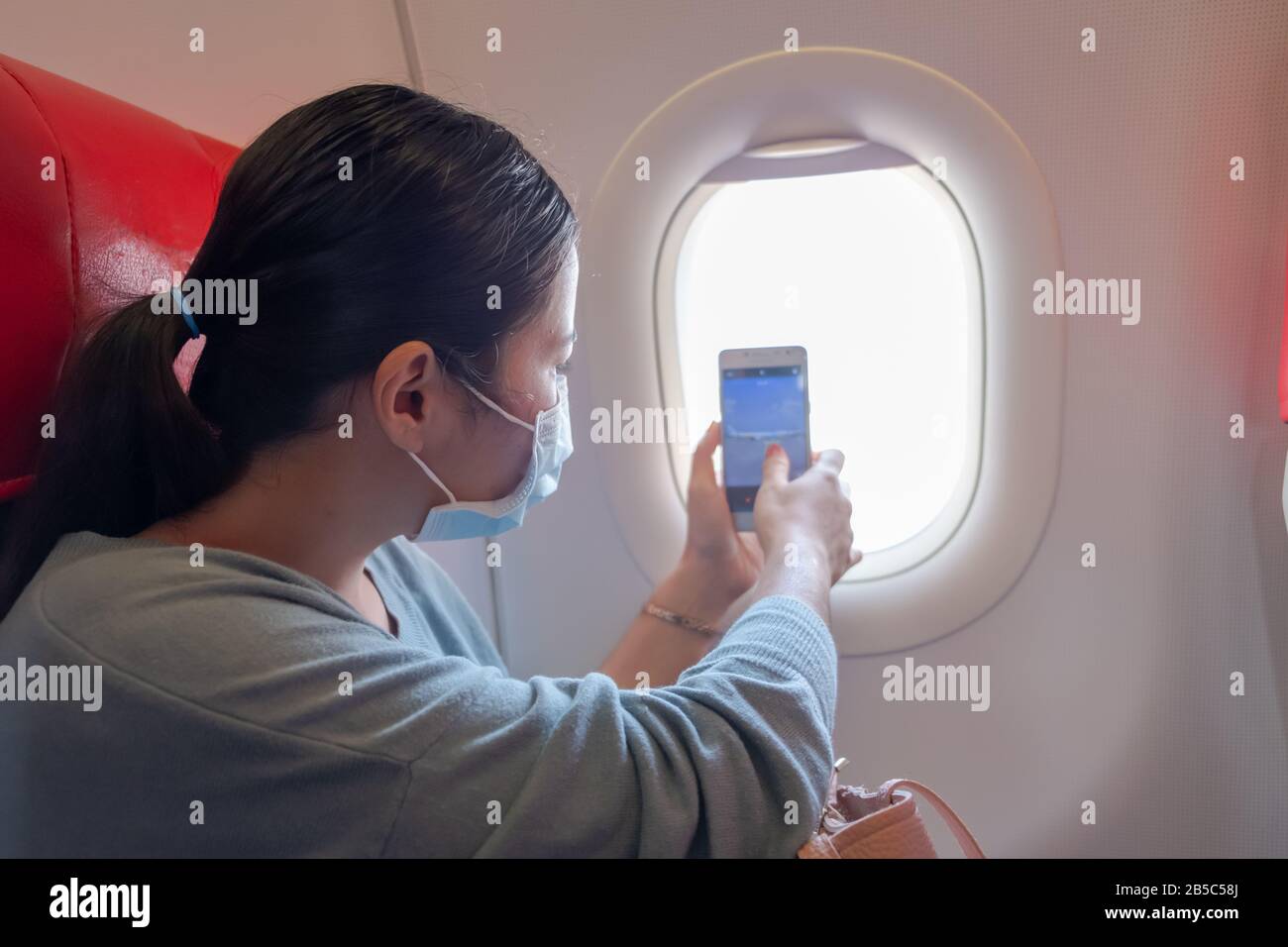 Asian girl use a protection mask for coronavirus or covid 19 in airport. Asian girl taking photos from the window of the plane. Stock Photo